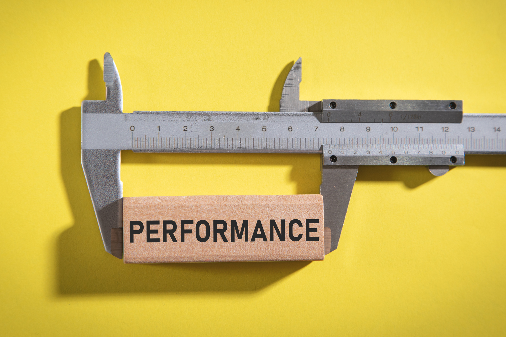 Vernier caliper with a Performance word on wooden block.