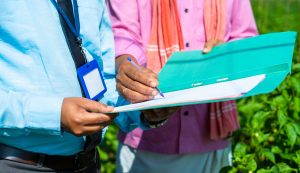 Close up shot of indian banker taking sign from farmer for loan agreement or contract documents at greenhouse - concept of banking support, agricultural loan and investment