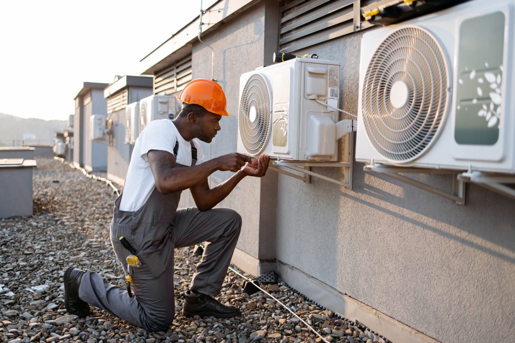 An in uniform worker inspecting air conditioner and using screwdriver during repairing work.