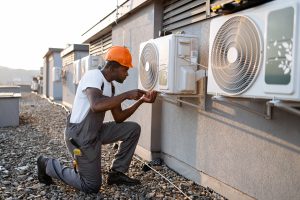 An in uniform worker inspecting air conditioner and using screwdriver during repairing work.