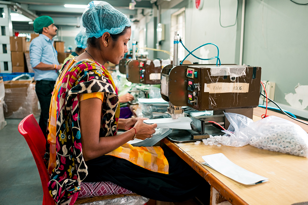 Indian woman at work using industrial equipment inside packaging manufacturing plant