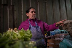 A woman at a market is talking and pointing.
