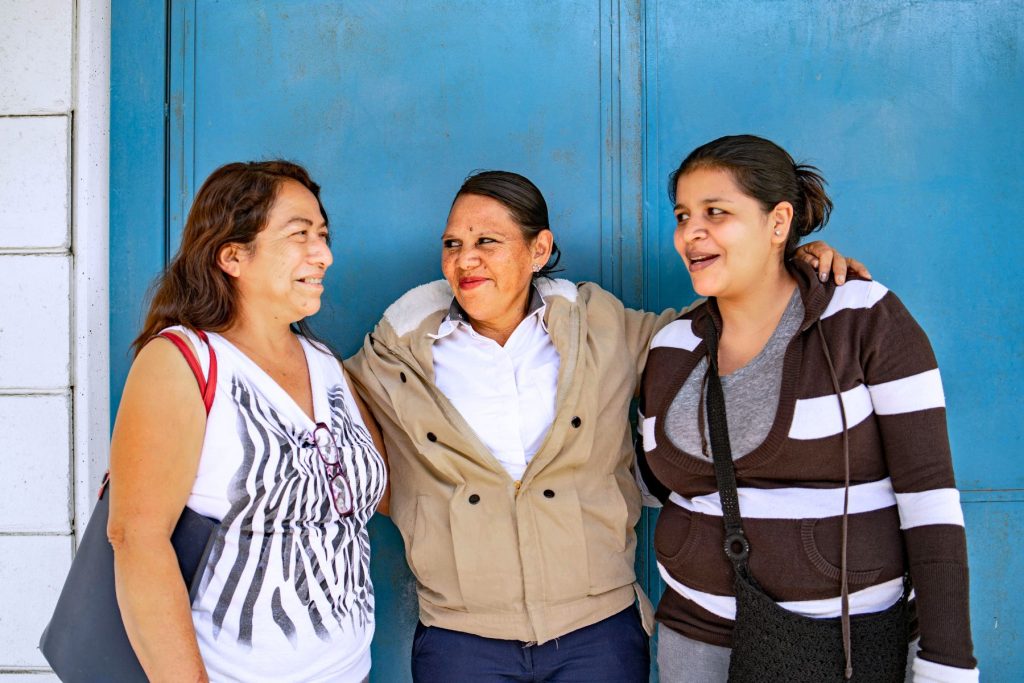 three latin women smiling in front of blue door