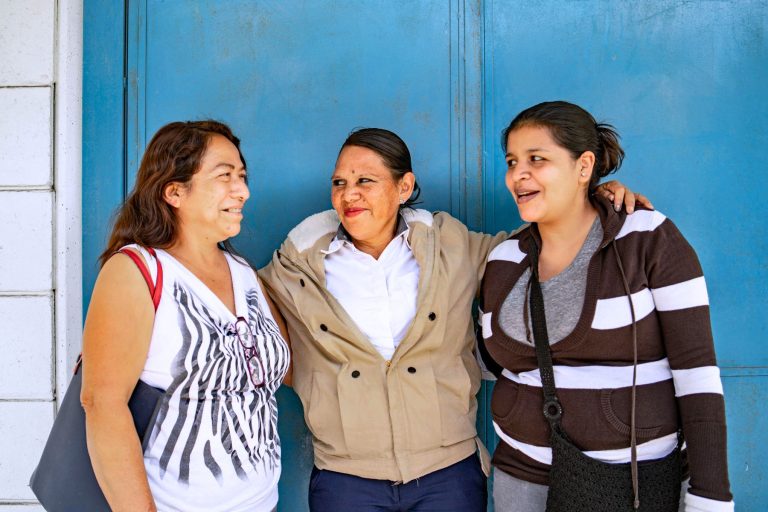 three latin women smiling in front of blue door